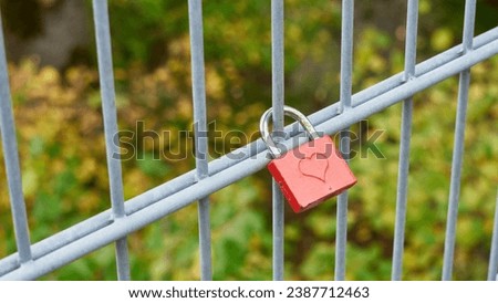 A red lock with closed hearts hangs on the bridge fence