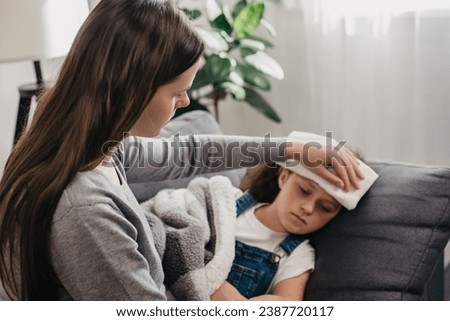 Selective focus of caring young mother put towel on head sick child girl with high body temperature lying on sofa at home. Mommy take care of ill little daughter. Childcare, kids healthcare concept Royalty-Free Stock Photo #2387720117