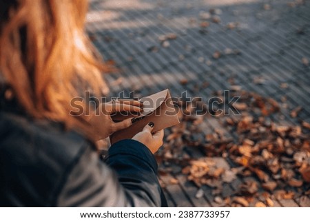 A woman closes an envelope in an autumn park on a bench. Female hands put the letter in the craft envelope. Woman holding a craft envelope Royalty-Free Stock Photo #2387733957