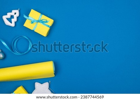New Year or Christmas background with gift box wrapped in yellow paper, balls, glitter on blue background with room for your festive message. 