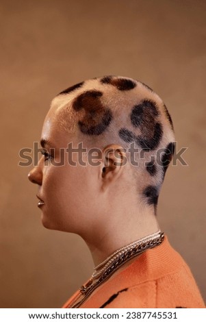 Side view portrait of young woman with buzzcut cheetah print against studio background