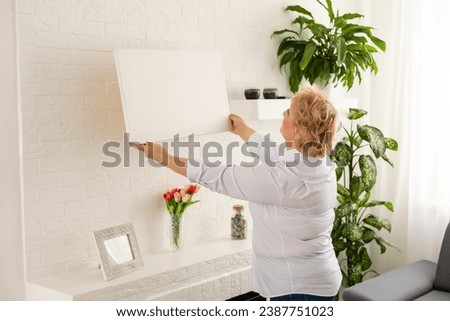 Picture of canvas. Blonde-haired elderly woman feeling motivated while taking picture of her creative canvas