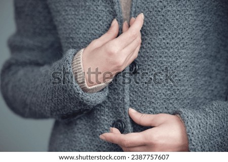 Close-up of a gray knitted jacket. Women's hands fasten buttons. Winter, autumn warm woolen clothes.