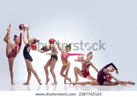 Group of beautiful little girls, children, rhythmic gymnasts in stage clothes dancing with balls against white studio background. Concept of choreography, hobby, art, sport, childhood, performance