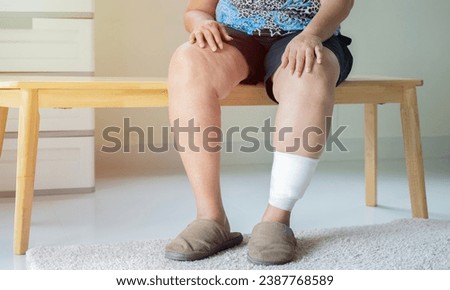 Shot of elder woman sitting on wooden chiar with injured leg. Wounds at the legs, bandages a legs wound pain medicine concept.