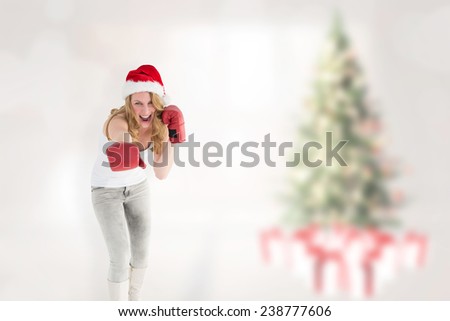 Festive blonde punching with boxing gloves against blurry christmas tree in room