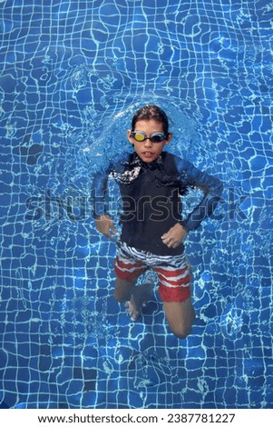 Photo of a young teenager handsome good looking male boy swimmer in a blue swimming pool alone with nobody around in the resort hotel during his holidays