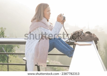Active asian woman holding camera and looking mountain view at countryside homestay in the morning sunrise with copy space. trip and relaxing. Travel vacations and lifestyle concept.