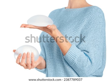 Woman holding and squeezing round implants on white background with clipping path. Mammoplasty and plastic surgery. Royalty-Free Stock Photo #2387789037