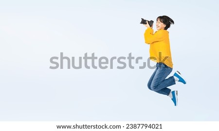 Asian woman wearing casual wear jumping energetically with digital camera. Girl photographer. Wide angle visual for banners or advertisements.