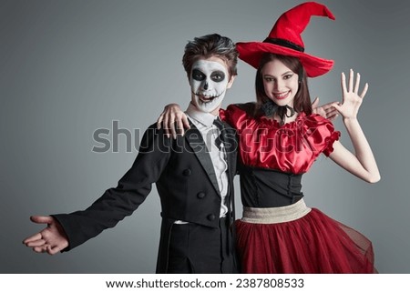 A teenage boy in a costume of sugar skull boy and a girl in a witch's costume posing together with fun at studio. Grey background with copy space. Halloween party for teenagers. 