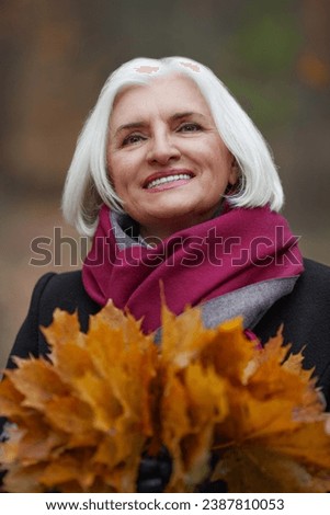 Close up Caucasian joyful gray haired old woman with autumn leaves smiling outdoors. Happy mature female Portrait of senior beautiful lady Enjoying life outdoors. Royalty-Free Stock Photo #2387810053