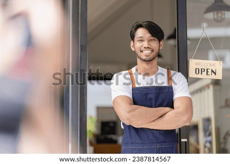 small business idea A smiling African American bakery worker in an apron stands outside a coffee shop with an open sign. Owner of a small coffee shop