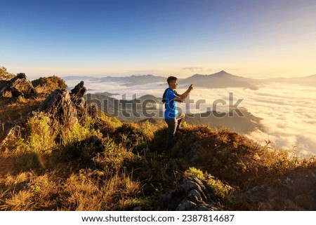 Traveler standing on the edge of the cliff holding smartphone taking a photo at the beautiful Doi pha tang mountain. Beautiful landscape sunrise mountain in Chiang rai , Northern of Thailand