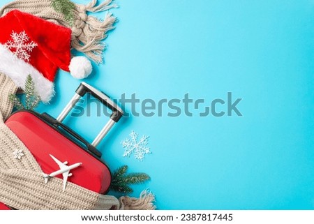 Christmas Soar: Top-view picture of a red suitcase, miniature airplane, Santa's clothing, and winter-themed elements on a bright blue backdrop, providing space for your holiday wishes