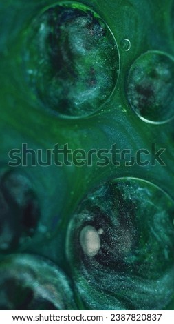 Abstract background. Shimmering mix. Magic liquid. Oil spill circles with purple metallic sparkling grain texture ink floating on green shiny substance surface.