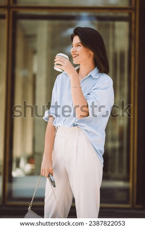 Photo of happy young woman in casual holding cup of coffee to go during morning in city