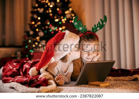 A happy children kissing and watching cartoons on tablet at home on new year and christmas eve.