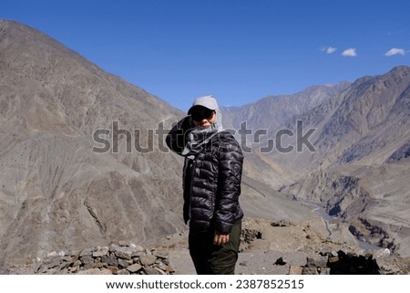 An Asian female tourist standing in front of the view of the dried, treeless high mountain ranges on the way towards Fairy Meadow, Karakoram Highway, Pakistan.