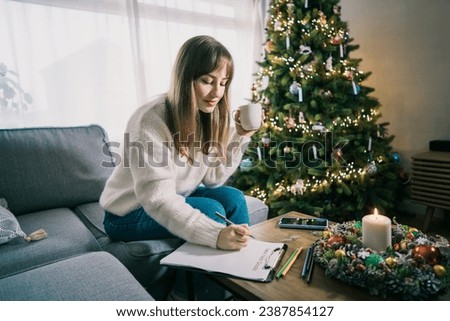 Young Woman with cup is hand writing New year's goals on note paper in new year day. New year resolutions list. Goals, resolutions, plans, action, checklist concept. New Year template, copy space Royalty-Free Stock Photo #2387854127