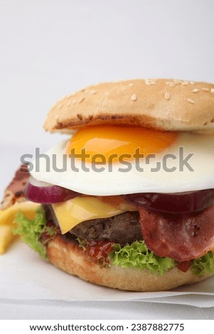 Delicious burger with fried egg on white tiled table, closeup