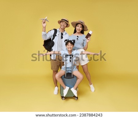 Happy fun asian family vacation portrait. Father, mother and daughters ready for travel flight with suitcase isolated on yellow studio background. Royalty-Free Stock Photo #2387884243