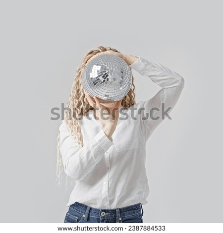 Woman holding mirror ball in front of face, grey background, no face trend concept. Female with long curly hair dreadlocks hiding behind sparkling lighting disco ball. Creative Celebration visual. 