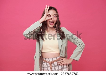 Portrait happy Asian teen woman shows ok hand sign and looking at the camera on pink background.