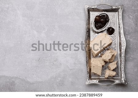 Pieces of tasty halva and dates served in vintage tea set on light grey table, top view. Space for text