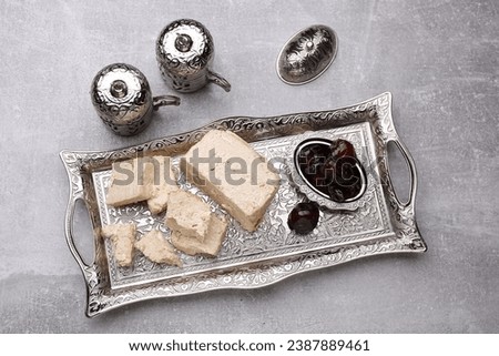Pieces of tasty halva and dates served in vintage tea set on light grey table, above view