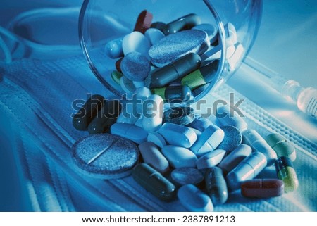 an overturned glass transparent glass on a medical disposable protective mask with colored pills , a photo in blue tones , the concept of medicine