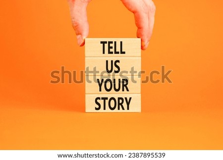 Tell us your story symbol. Concept word Tell us your story on beautiful wooden block. Beautiful orange table orange background. Businessman hand. Business tell us your story concept. Copy space.