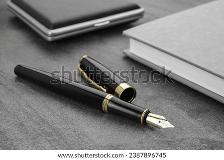 Stylish black fountain pen, notebook and cigarette case on grey textured table, closeup