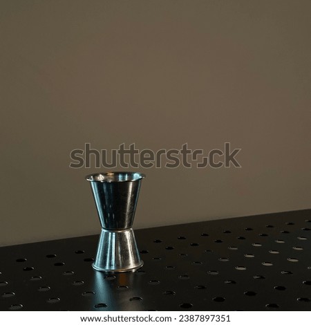 Stylish metal jigger at the bar at background of painted wall. One object. Minimalism picture. Bar tender’s staff