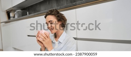 Beauty and women concept. Relaxed young woman enjoys her cup of tea. Girl sits on floor in kitchen with pink mug, drinks coffee and smiles from delight.