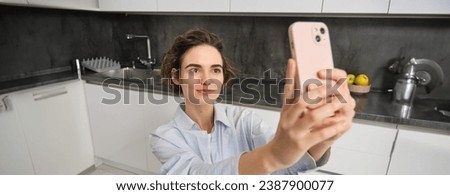 Portrait of beautiful young woman, taking selfie on mobile phone at home, poses for photo with smartphone.