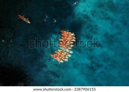 Captain boat sails towards a row of kayaks in the deep turquoise sea. Top view
