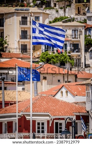 Greek Flag Waving Over Picturesque Coastal Town of Parga, Greece. European Union Flag and Traditional House Rooftops in Background.