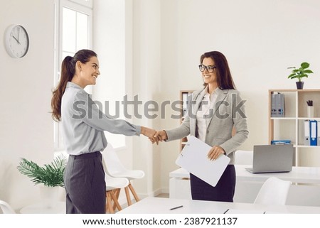 Young happy smiling business women standing in office on workplace shaking hands with each other reaching agreement and making a good deal or signing a contract. Business people at work.