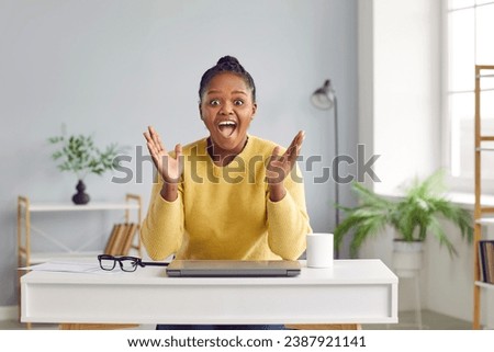 Shocked surprised young african american woman sitting at the desk with laptop at home waving hands looking at camera during online video conference call. Concept of internet communication, blogging. Royalty-Free Stock Photo #2387921141