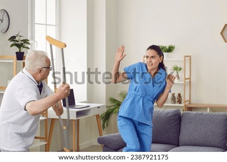 Senior patient showing aggression toward medical worker. Old man wakes up in bad mood, starts fight with hospital staff, threatens nurse with crutch and gets very angry, dangerous and uncontrollable Royalty-Free Stock Photo #2387921175