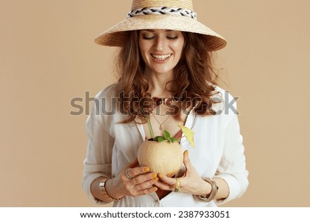 Beach vacation. happy modern middle aged housewife in white blouse and shorts isolated on beige with coconut cocktail and summer hat.