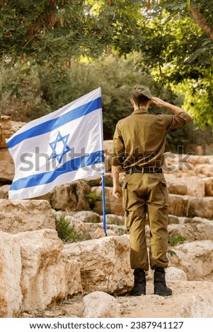 Israeli soldier stands in a field with Flag of Israel in the blooming desert. Concept Jewish patriot, IDF, Memorial Day for the Fallen Soldiers of the Wars, Israel Independence Day Royalty-Free Stock Photo #2387941127
