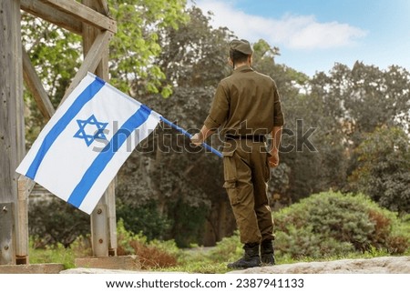 Israeli soldier stands in a field with Flag of Israel in the blooming desert. Concept Jewish patriot, IDF, Memorial Day for the Fallen Soldiers of the Wars, Israel Independence Day Royalty-Free Stock Photo #2387941133