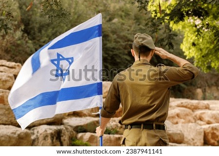 Israeli soldier stands in a field with Flag of Israel in the blooming desert. Concept Jewish patriot, IDF, Memorial Day for the Fallen Soldiers of the Wars, Israel Independence Day Royalty-Free Stock Photo #2387941141