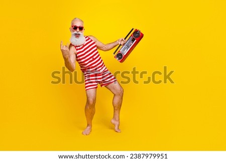 Full length photo of aged man in swimsuit positive singing metal rock roll brutal music holding boombox isolated on yellow color background