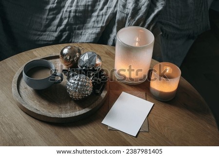 Moody cozy winter home, interior still life. Cup of coffee, vintage Christmas ornaments, balls on round wooden table. Blurred background. Candles in colorful glass candleholders. Blurred background.