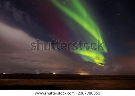 Aurora borealis over snow covered hillside in wintery surroundings. Icelandic northern lights are magnificent spectacle of nature, shining the nighttime sky in an icy landscape. Royalty-Free Stock Photo #2387988353