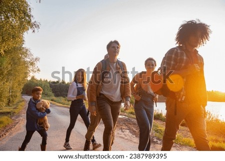A group of friends, boys and girls, tourists with a little boy walk along the shore of the lake against the backdrop of the setting sun at Golden Hour, high quality photo