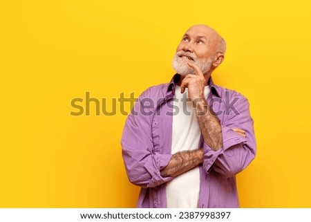 pensive old bald grandfather with gray beard in purple shirt stands with his arms crossed on yellow isolated background and thinks, elderly pensioner dreams and plans and looks away Royalty-Free Stock Photo #2387998397
